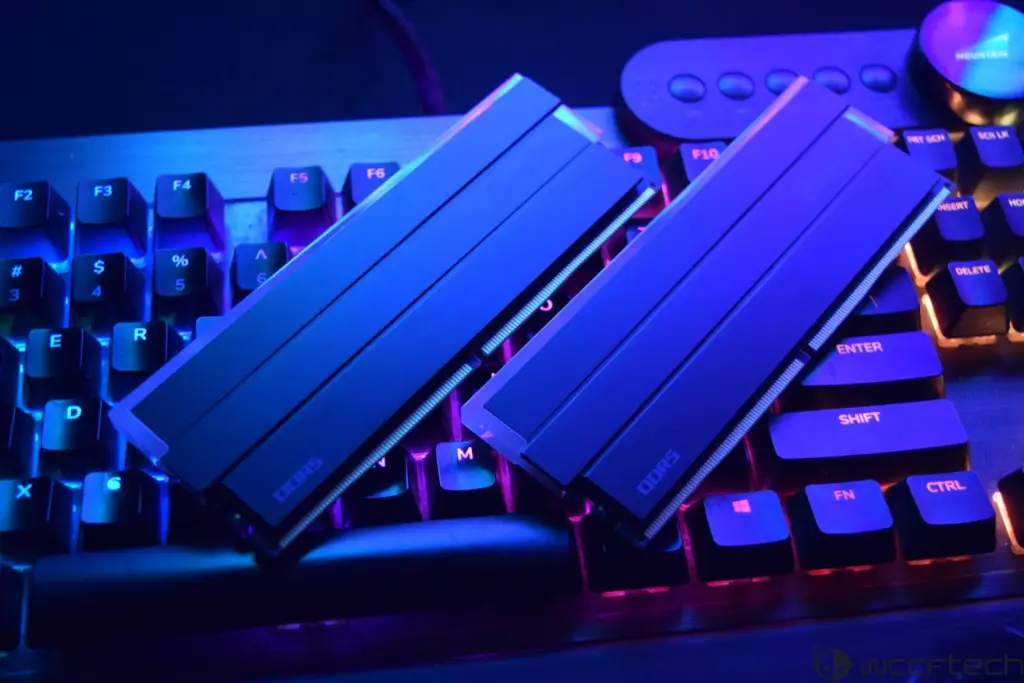 Two DDR5 RAM sticks lying on a backlit mechanical keyboard with visible QWERTY keys and a mountain logo in a dark blue and purple lighting environment.