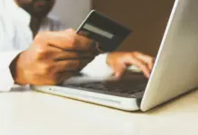 رجل يمسك بطاقة دفع أمام حاسوب محمول أثناء التسوق عبر الإنترنت
