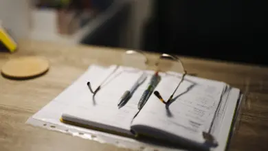 دفتر ملاحظات مفتوح وقلمان ونظارة على مكتب خشبي