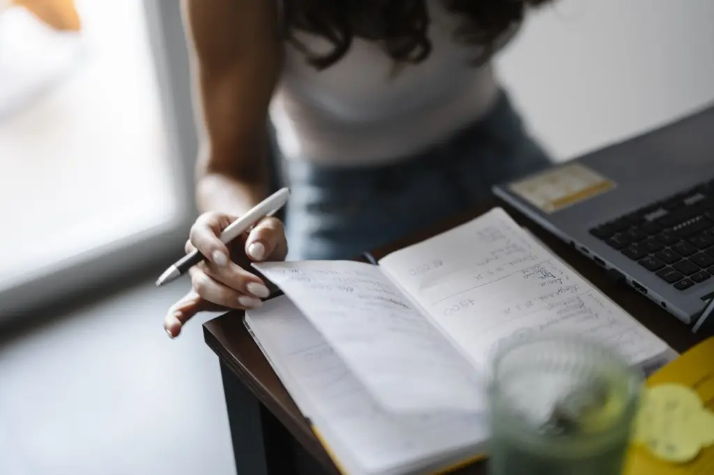 شخص يكتب في دفتر بجانب حاسوب محمول