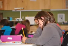 تلميذة تكتب في دفتر على طاولة في صف دراسي