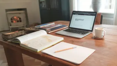 جهاز محمول بمستند مفتوح على مكتب خشبي بجانب دفاتر وكوب