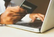 يد تحمل بطاقة دفع أمام جهاز محمول