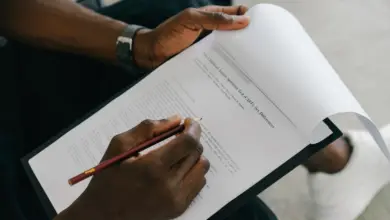 يد تمسك قلمًا وتكتب على مستند مثبت في لوح كتابة