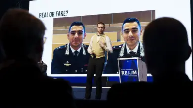 شاشة في مؤتمر تعرض صورة مع عبارة حقيقي أم مزيّف حول التزييف العميق