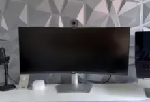 شاشة Dell منحنية عريضة على مكتب أبيض بجانب ميكروفون وكاميرا ويب