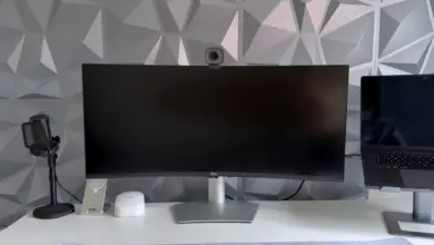 شاشة Dell منحنية عريضة على مكتب أبيض بجانب ميكروفون وكاميرا ويب