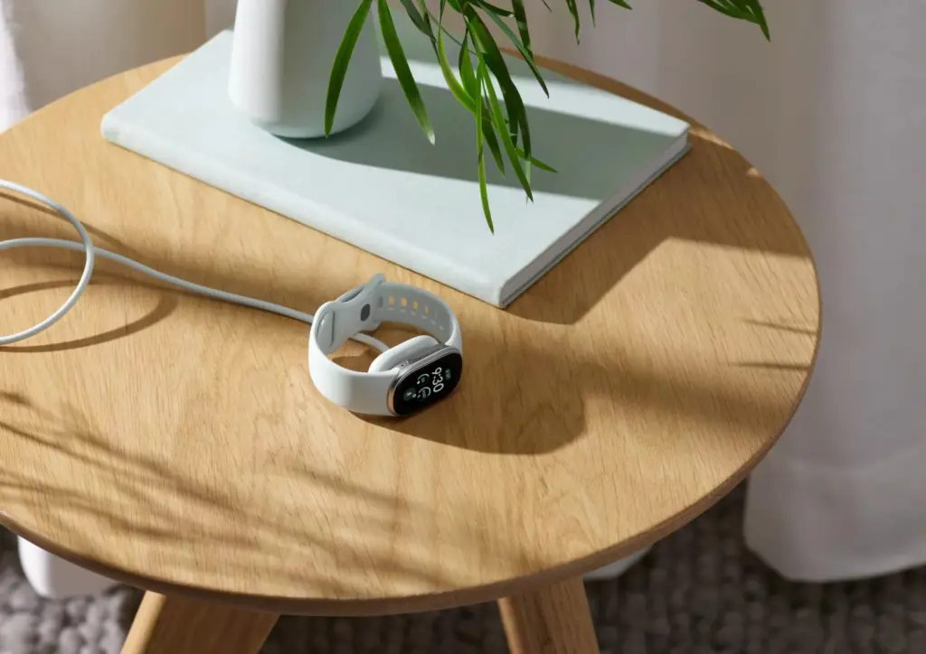 سوار Fitbit Edge موضوعًا على طاولة بجانب كابل الشحن المغناطيسي