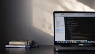 حاسوب محمول على مكتب مع كتب وشاشة تعرض بيئة عمل
