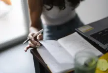 شخص يكتب في دفتر على مكتب بجانب لابتوب