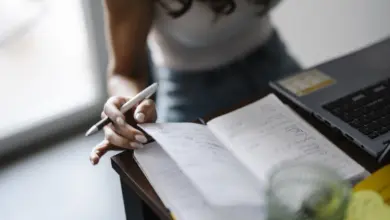 شخص يكتب في دفتر على مكتب بجانب لابتوب