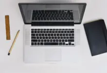 لابتوب ماك على مكتب بجانب دفتر وقلم