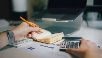 دفتر وآلة حاسبة ومخططات على مكتب أمام جهاز محمول