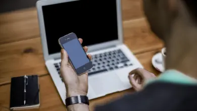 رجل يمسك جوالًا أمام لابتوب مفتوح