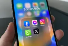 يد تمسك هاتفًا تظهر عليه أيقونات تطبيقات التواصل الاجتماعي ومنها Instagram