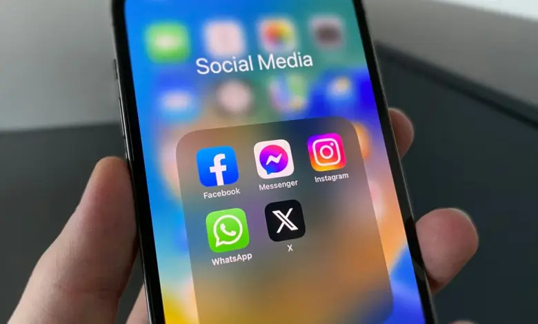 يد تمسك هاتفًا تظهر عليه أيقونات تطبيقات التواصل الاجتماعي ومنها Instagram