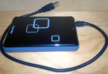 قرص خارجي أسود متصل بكابل USB على سطح خشبي