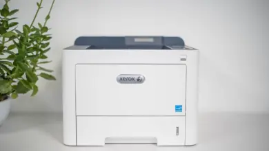 طابعة ليزر Xerox بيضاء على رف أبيض بجانب نبتة